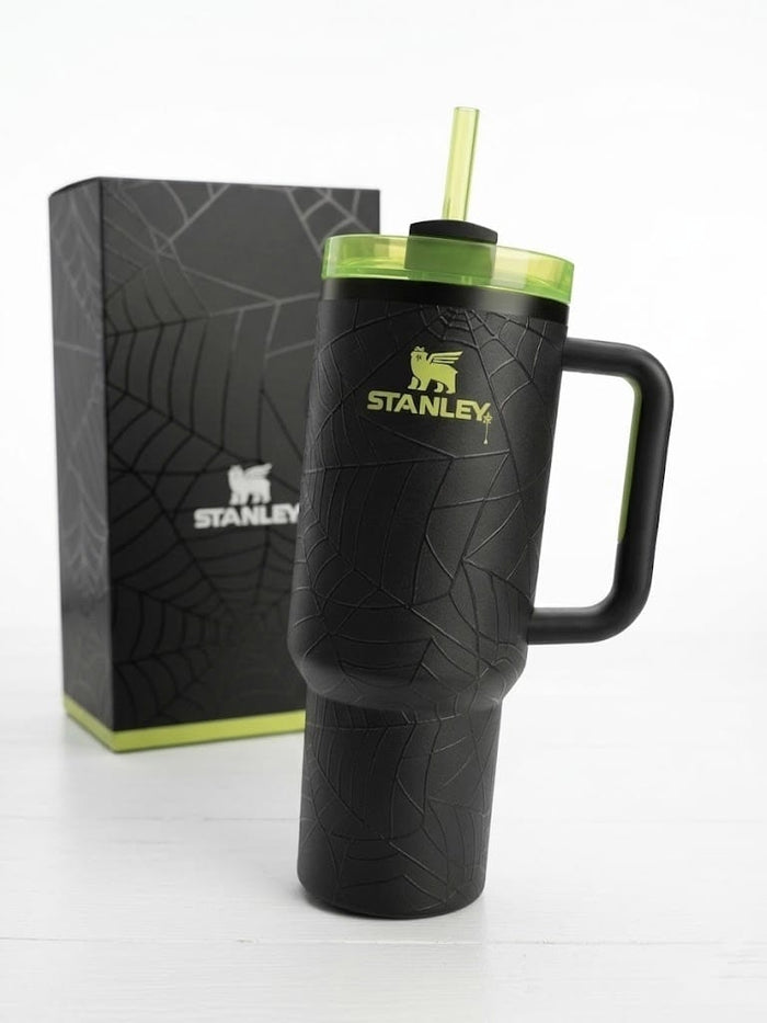 A black Stanley insulated tumbler with a handle, textured crackle pattern, and a translucent green lid with a straw, shown next to its black branded box on a white background.